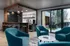 Chic apartment community lounge featuring modern teal armchairs, stylish bar with pendant lighting, and floor-to-ceiling windows overlooking a serene courtyard.