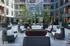 Modern apartment courtyard featuring cozy wicker seating around a sleek fire pit, surrounded by lush greenery and stylish outdoor decor.