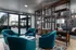 Elegant apartment lounge with stylish teal armchairs, modern shelving, and floor-to-ceiling windows opening to a spacious patio.