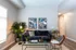 Modern living room with cozy grey couch, decorative plants, and vibrant artwork. Elegant interior featuring a sleek glass coffee table and stylish lighting.