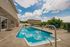 Inviting outdoor pool at a modern apartment complex, surrounded by comfortable seating areas and lush greenery under a bright blue sky.