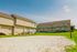 Inviting townhouse complex with beige siding and charming porches, surrounded by lush green grass and a sandy outdoor recreation area, under a clear blue sky.