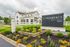 Charming white building with elegant architecture at The Gramercy, New Albany, surrounded by vibrant landscaped gardens under a cloudy sky.