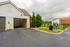 Inviting garage entrance with exterior lighting, surrounded by lush greenery and a well-maintained driveway, perfect for easy vehicle access.