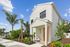 Charming modern home with a vibrant orange door, surrounded by lush tropical landscaping and tall palm trees under a clear blue sky.