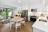 Bright and airy open-plan kitchen and living area with modern decor, large sliding glass doors, and a view of a lush green garden.