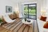 Chic living room with sleek white furniture, striped rug, and sliding glass doors opening to a lush green patio view.