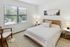 Bright and inviting bedroom with a cozy wooden bed, soft lighting, and a large window offering serene outdoor views.