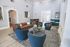 Elegant and spacious living area featuring a stylish brown leather sofa, vibrant blue chairs, and a chic coffee table. The room is enhanced by modern decor, a cozy corner booth, and abundant natural light.