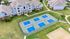 Aerial view of modern apartment complex with vibrant blue tennis courts, surrounded by lush green lawns and walking paths.