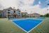 Charming apartment complex with stylish architecture, featuring vibrant blue tennis courts under a picturesque sky.