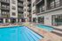 Modern apartment complex with a luxurious pool area featuring sun loungers and vibrant blue umbrellas, offering a perfect relaxation spot.