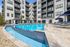 Luxurious apartment complex featuring a sparkling outdoor pool, elegant lounge chairs, and stylish blue umbrellas, perfect for relaxation and leisure.