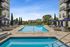 Luxurious apartment complex pool area with modern loungers, elegant umbrellas, and pristine water, surrounded by lush greenery and scenic views.