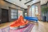 Chic living room with an elegant orange tufted sofa, vibrant blue dresser, and large arched windows, exuding style and sophistication.