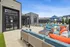 Chic outdoor lounge area showcasing stylish wicker furniture with vibrant cushions, poolside recliners, and elegant blue umbrellas against a modern apartment backdrop.