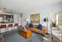 Chic living room with a modern brown leather sofa, stylish floor lamp, and open layout leading to the kitchen with bar seating and contemporary lighting fixtures.