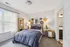 Cozy and elegant bedroom with stylish decor, featuring a plush bed with navy bedding, unique wall art, and ample natural light from large windows.
