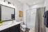 Modern bathroom with elegant black cabinetry, bright lighting, and artistic wall decor; featuring a sleek shower and stylish fixtures.