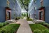 Charming apartment complex with blue brick exterior, lush greenery, and a welcoming landscaped walkway.