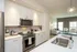 Modern apartment showcasing a sleek kitchen with stainless steel appliances, smooth white cabinetry, and open view to a bright living area with comfortable seating.