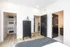 Modern bedroom with sleek black dresser, spacious walk-in closet, and hardwood floors, leading to a bathroom with stylish decor.
