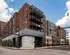 Modern urban apartment building with stylish brick facade and large windows, located at a busy city intersection.