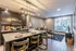 Chic open-plan kitchen and living space with elegant lighting, stylish bar seating, and a cozy lounge area, bathed in natural light from large windows.