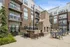Elegant apartment complex courtyard featuring a stylish outdoor seating area with a brick fireplace, surrounded by lush greenery and string lights, creating an inviting atmosphere.