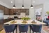 Modern kitchen with elegant pendant lighting, stylish cabinetry, and a spacious island with seating, adjacent to a cozy bedroom featuring plush bedding and a bright, welcoming atmosphere.