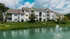 Charming apartment complex with white exteriors, lush landscaping, and a serene pond with a central fountain.