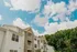 Charming apartment building with classic stone and white panel exterior under a bright blue sky, surrounded by lush greenery.