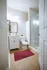 Elegant bathroom with modern fixtures, featuring a glass-enclosed shower, stylish vanity, and hardwood flooring complemented by a rich burgundy rug.