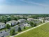 Aerial view of charming apartment complex surrounded by lush greenery, showcasing ample parking space and serene suburban landscape.