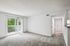 Bright and airy living room with plush carpet, modern patio door leading to a lush green view, and sleek hallway access.