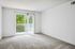 Bright, airy room with a large sliding glass door opening to a private balcony, featuring lush green views and plush carpeting, perfect for relaxation.
