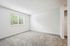 Bright, spacious bedroom with plush carpeting and large window overlooking green foliage.