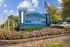 Elegant entrance sign for Residences at Central Park, surrounded by vibrant flowers and greenery under a sunny sky.