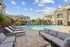 Inviting apartment pool area with modern lounge chairs, lush landscaping, and elegant architecture under a bright blue sky.