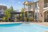 Inviting apartment complex showcasing a sparkling pool, outdoor seating, and charming architecture under a sunny sky.