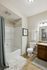 Bright and modern bathroom with elegant fixtures, cozy white rug, stylish framed artwork, and inviting shower area.