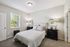 Inviting bedroom with plush carpeting, elegant furnishings, and ample natural light from a large window.