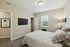 Inviting bedroom with elegant bedding, a flat-screen TV, and ample natural light from large window, perfect for relaxation.