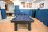 Modern entertainment room featuring a sleek pool table, stylish blue paneling, and a chic kitchenette with geometric wall tiles.