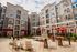 Modern apartment complex exterior showcasing stylish multi-story buildings with balconies, a vibrant outdoor courtyard with seating and tables, and lush landscaping under a sunny sky.