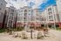 Modern apartment complex showcasing a vibrant courtyard with stylish seating and lush greenery against a backdrop of sleek architecture under a bright blue sky.