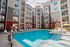 Modern apartment complex with a sparkling outdoor pool, comfortable lounge chairs, and vibrant umbrellas, offering a luxurious and relaxing retreat.