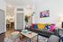 Chic apartment living room showcasing modern decor with colorful pillows, elegant floor lamp, and a cozy seating area opening to a stylish kitchen.