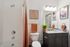 Modern bathroom with a sleek granite countertop, vibrant orange accents, and stylish art. Features a bathtub-shower combo and warm lighting.
