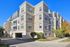 Elegant modern apartment building with spacious balconies, surrounded by lush greenery and blue skies.